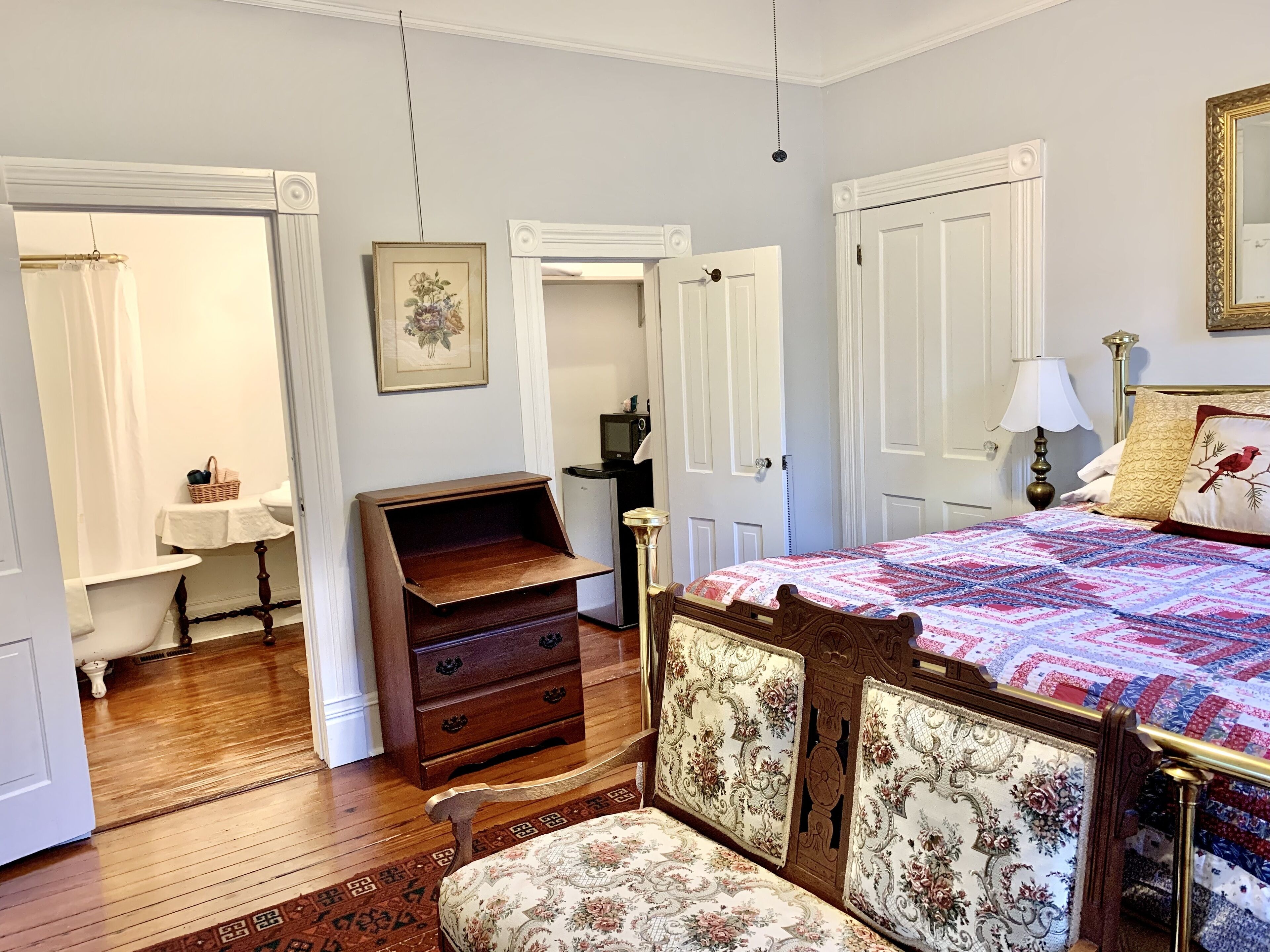 A bedroom with a bed, dresser, vanity, and a door leading to another room.