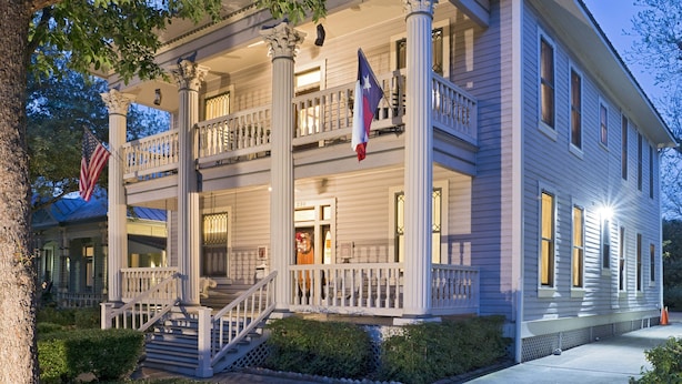 A two-story building with a porch, a flag, and a staircase leading to the entrance.
