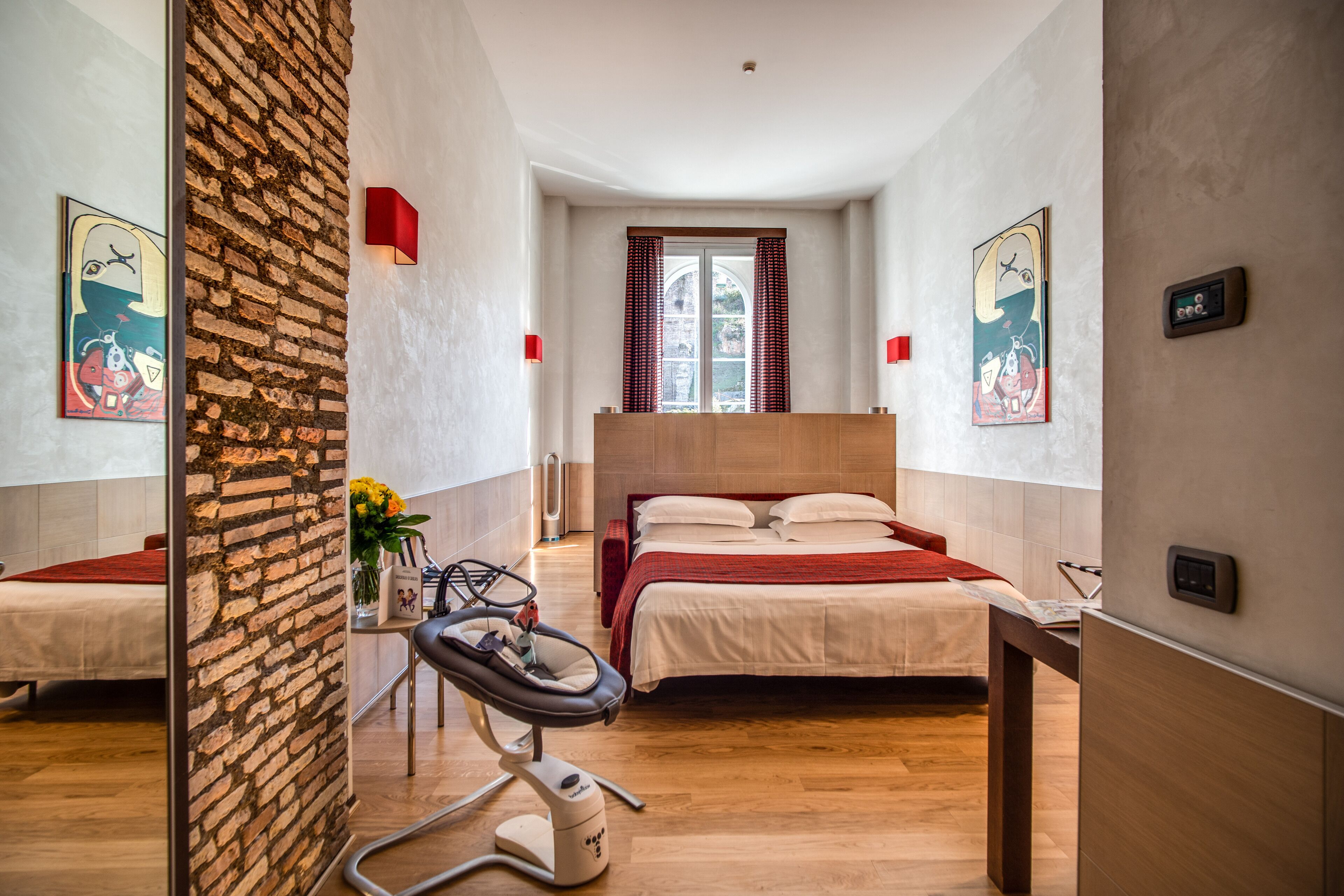 A hotel room with a bed, a chair, a window, and artwork on the walls.