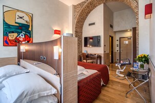 A hotel room with two beds, a desk, a chair, a TV, and a bathroom visible through an archway.