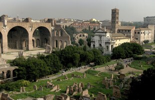Ancient ruins with arches and a tower, surrounded by greenery and historical buildings.