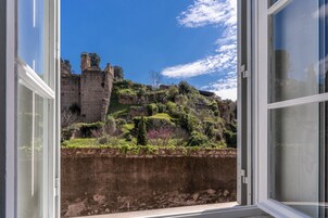 Vista a través de una ventana que muestra un muro de piedra histórico y una estructura similar a un castillo en la distancia.