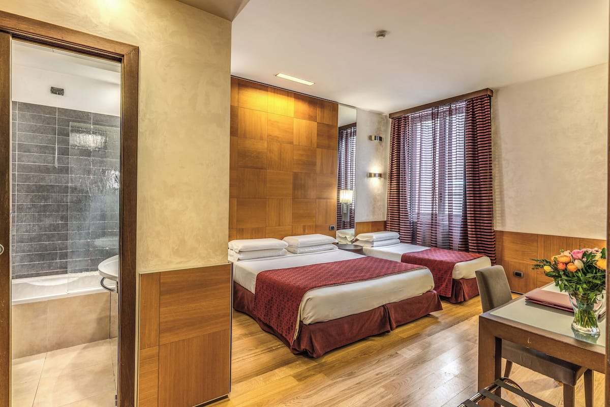 Una habitación de hotel con dos camas, un baño con ducha y un comedor con mesa y sillas.
