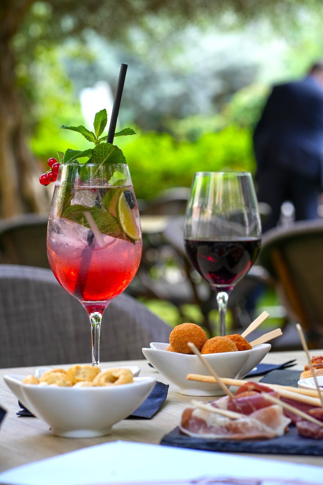 A table with a drink, a glass of red wine, and food items.