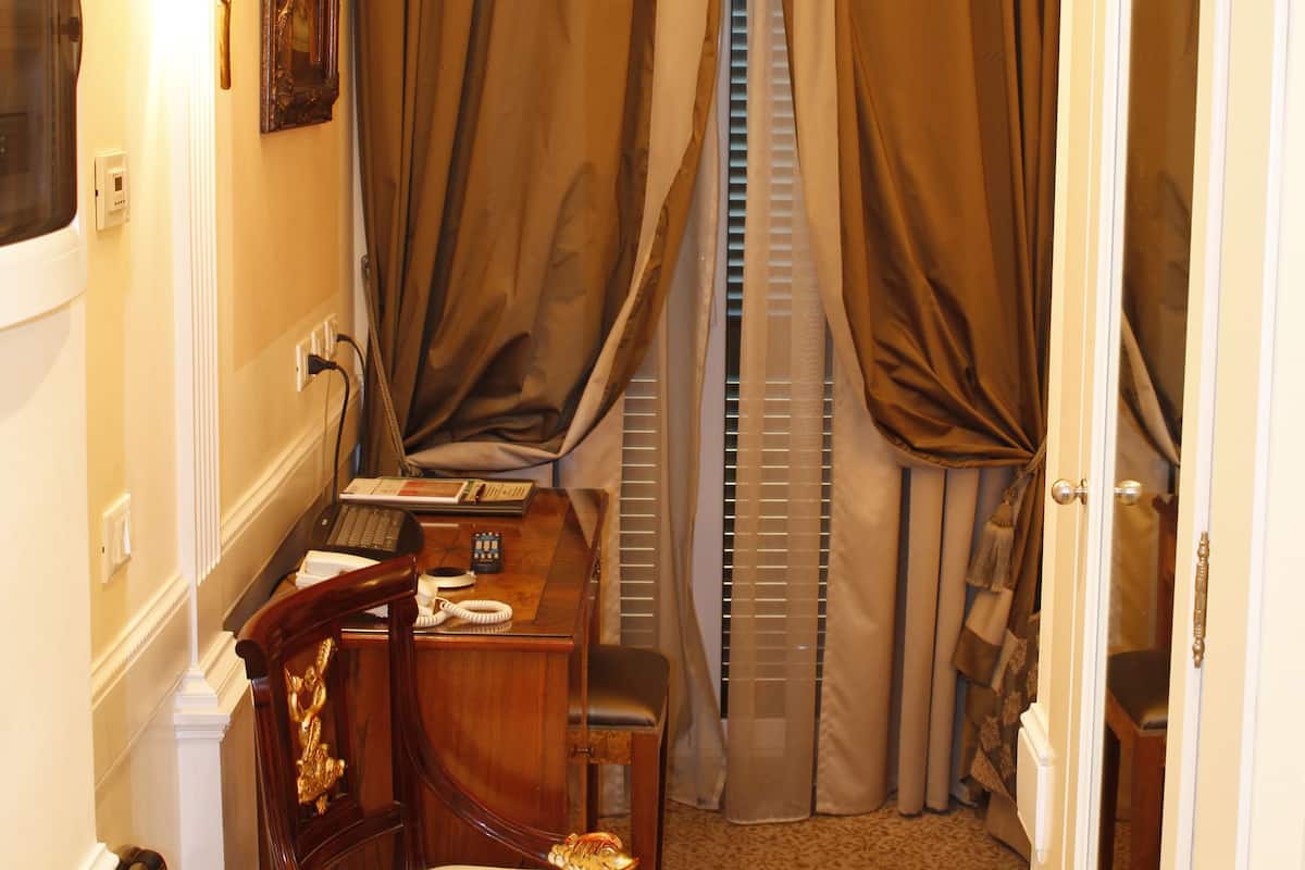 Una habitación de hotel con escritorio, silla y ventana con cortinas.