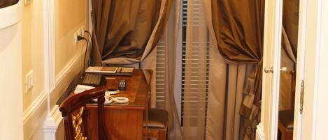 A hotel room with a desk, chair, and a window with curtains.