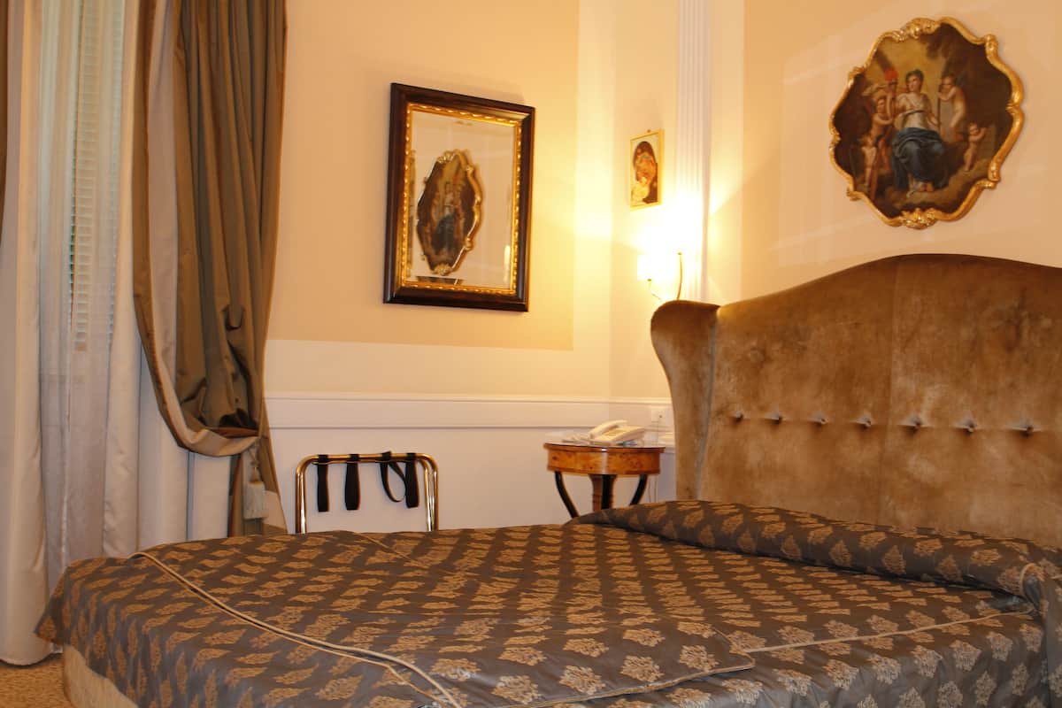 Una habitación de hotel con una cama grande, cabecera, mesita de noche y un cuadro en la pared.