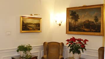 Una habitación con un cuadro grande de un paisaje, un sillón cómodo y una mesita con una planta en maceta.