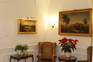 A room with a large framed landscape painting, a comfortable armchair, and a small table with a potted plant.