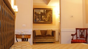 A hotel room with a bed, a sofa, a chair, a lamp, a painting on the wall, and a small table. - Boutique Hotel Trevi (Rome)
