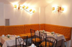 A corner dining area with orange cushioned booths, white tablecloths, and black chairs.