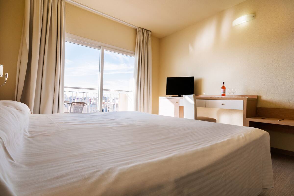 Une chambre d’hôtel avec un grand lit, un bureau avec une télévision et une bouteille de vin.