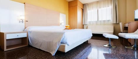 A hotel room with a bed, a desk, a chair, and a television.
