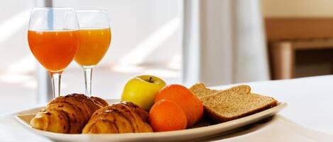 A breakfast plate with croissants, an apple, an orange, and two glasses of orange juice on a white tablecloth.