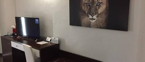 Habitación de hotel con un escritorio, una computadora, una silla y un cuadro grande de un puma en la pared.