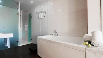 Un baño moderno con una bañera grande, cabina de ducha con vidrio y un lavabo blanco.