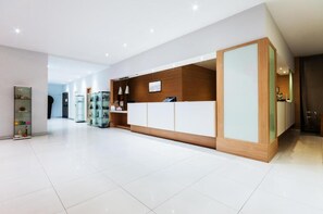 Una moderna zona de recepción con un expositor de vidrio, un mostrador de madera y un suelo de baldosas blancas.