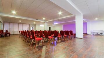 Un salón amplio con filas de sillas rojas, piso de baldosas y una pared iluminada en morado.