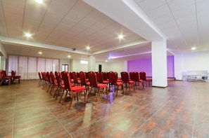 Une grande salle avec des rangées de chaises rouges, un sol carrelé et un mur illuminé de lumière violette.