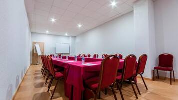 Un salón de conferencias con una larga mesa, sillas rojas y una pizarra.