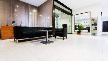 Una zona de recepción moderna con un sofá negro, un escritorio de madera y una vitrina de cristal.