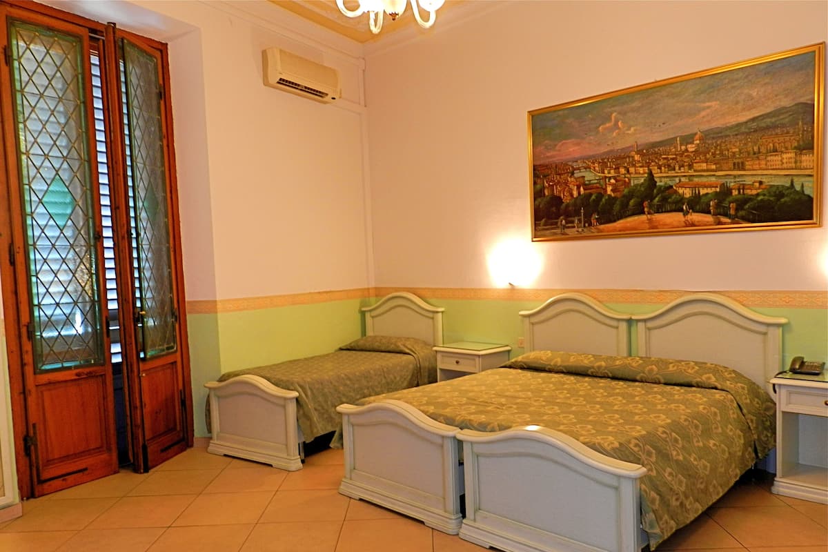 Une chambre avec deux lits simples et un lit double, un tableau au mur et une porte à panneaux de verre.