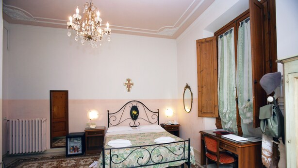A bedroom with a bed, a desk, a chair, a dresser, a mirror, a chandelier, and a radiator. - Hotel Desirée (Florence)