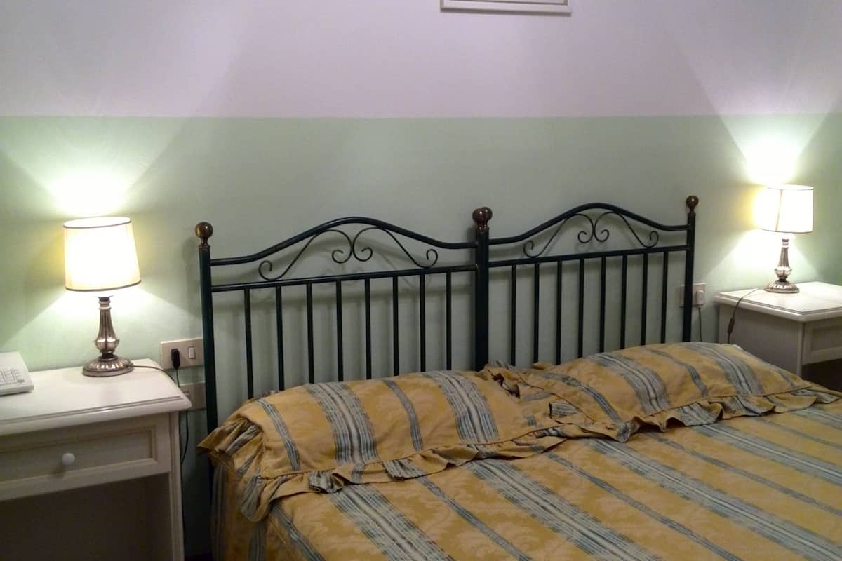 Une chambre à coucher avec un lit, deux tables de chevet, une lampe sur chaque table, un tableau encadré au mur et une petite table de nuit avec un téléphone.