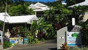 A sign for Palm Cove Tropic Apartments with a tropical garden and white buildings in the background. - Palm Cove Tropic Apartments (Palm Cove)
