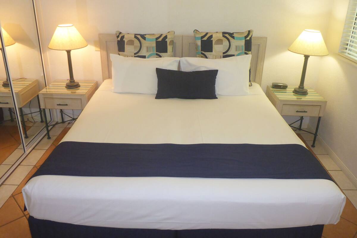 A neatly made bed with white and navy bedding, two bedside lamps, and a patterned headboard.