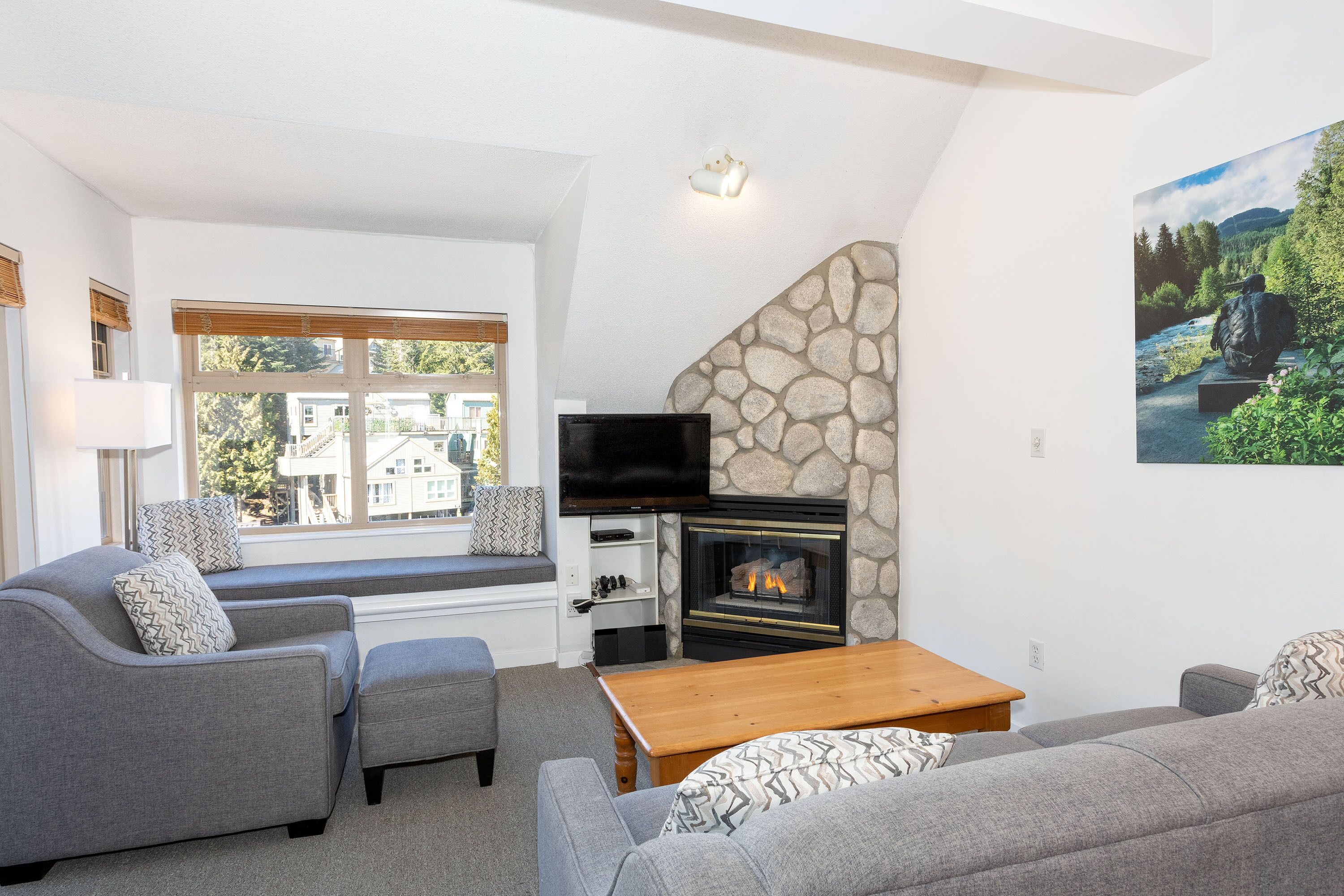 A living room with a stone fireplace, grey sofas, a wooden coffee table, and a television mounted above the fireplace.