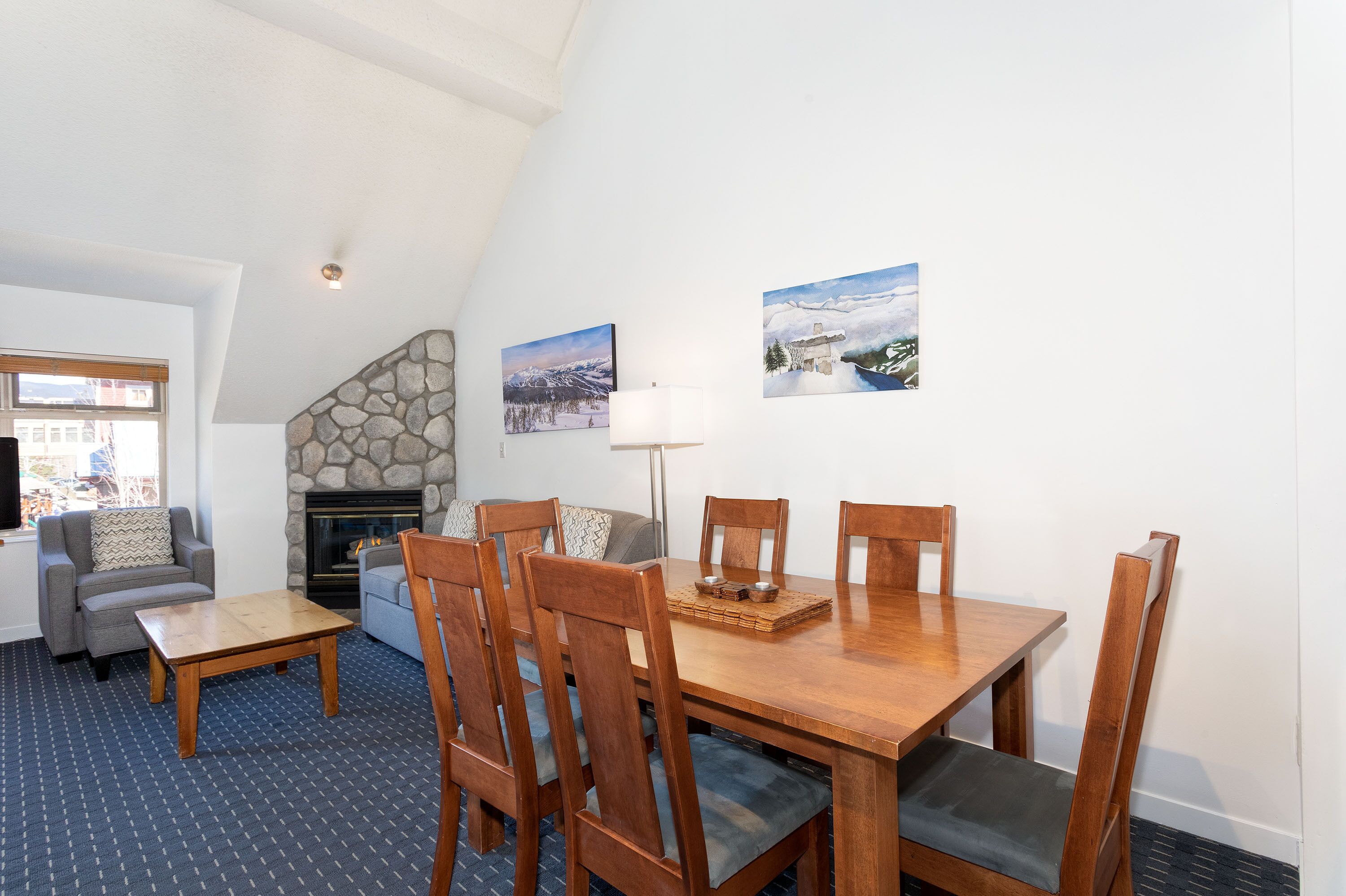 A dining area with a wooden table and chairs, a fireplace, and two wall-mounted paintings.