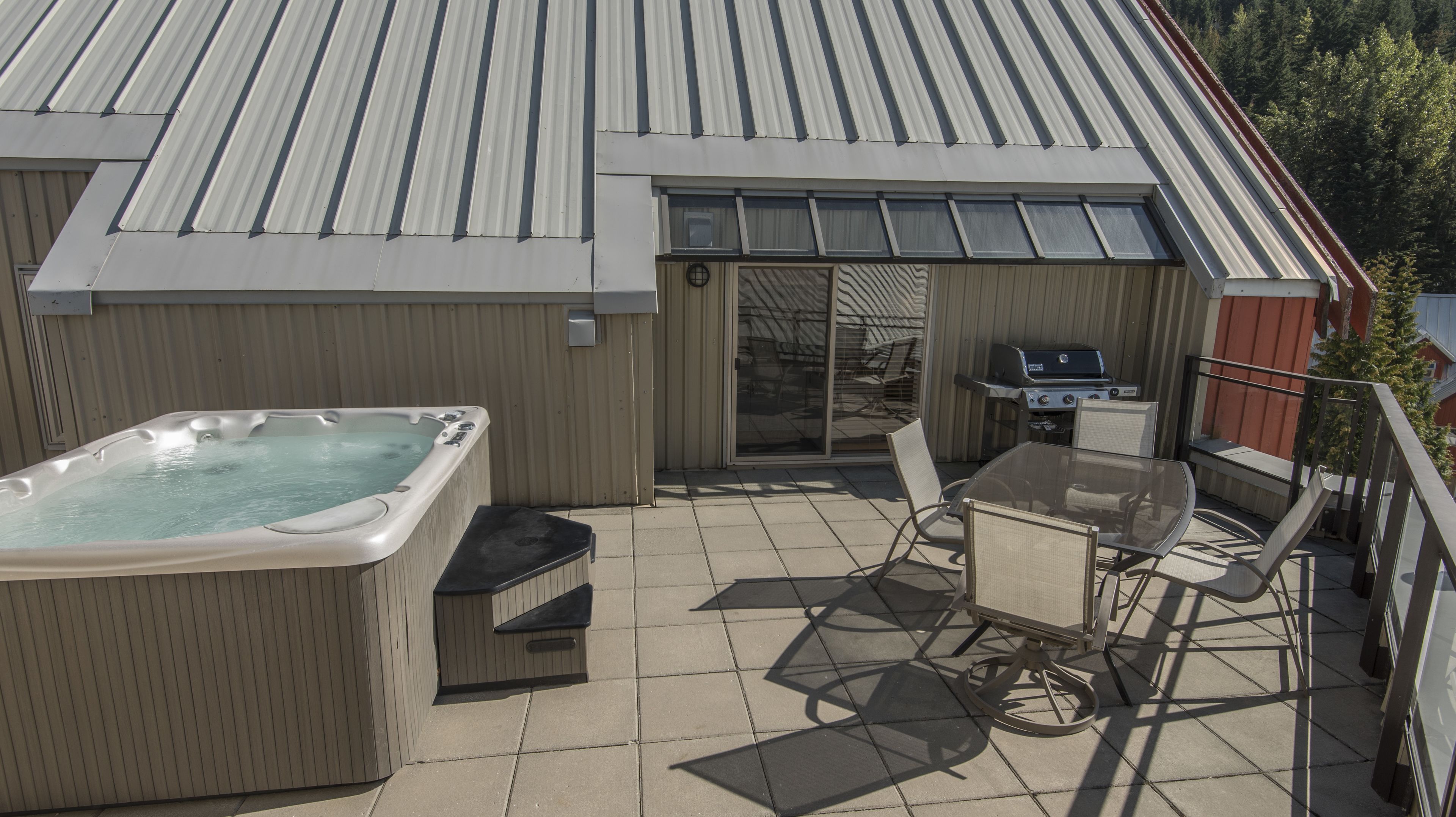 Une terrasse avec un jacuzzi, un barbecue et du mobilier d’extérieur.