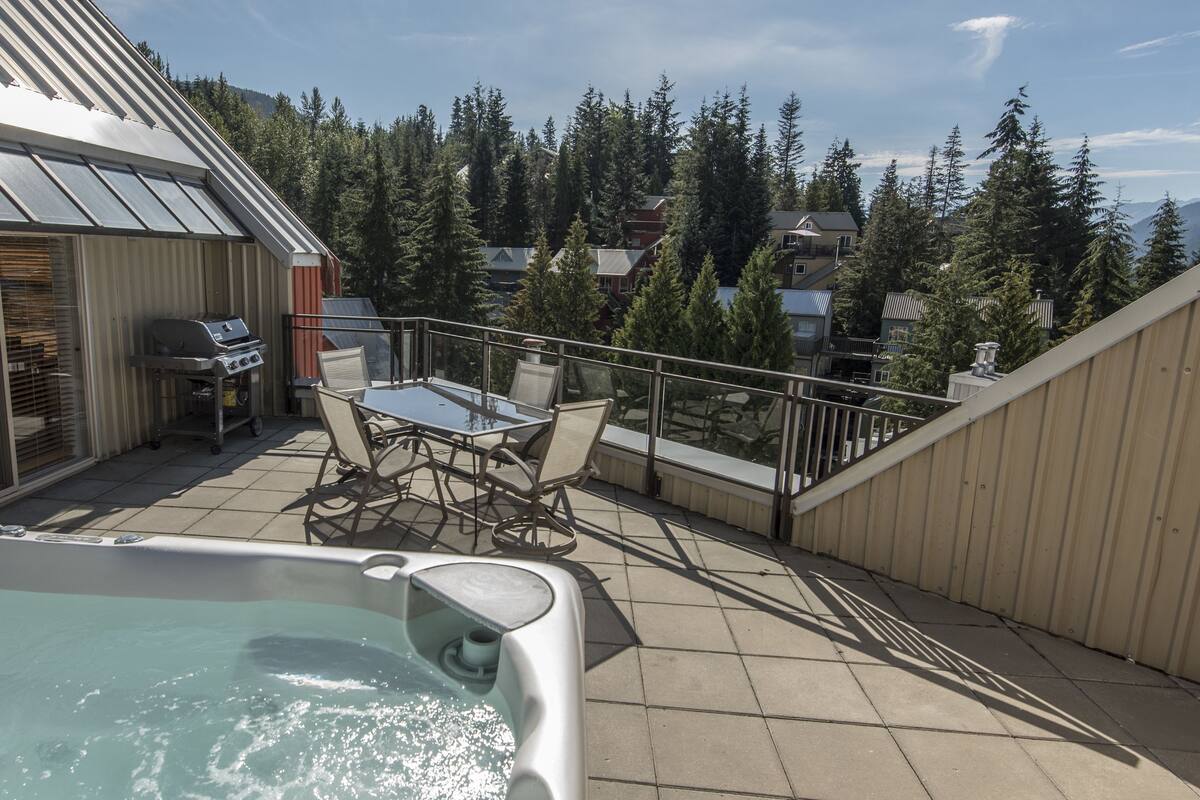 Une terrasse sur le toit équipée d’un jacuzzi, d’un barbecue et d’une table avec des chaises.
