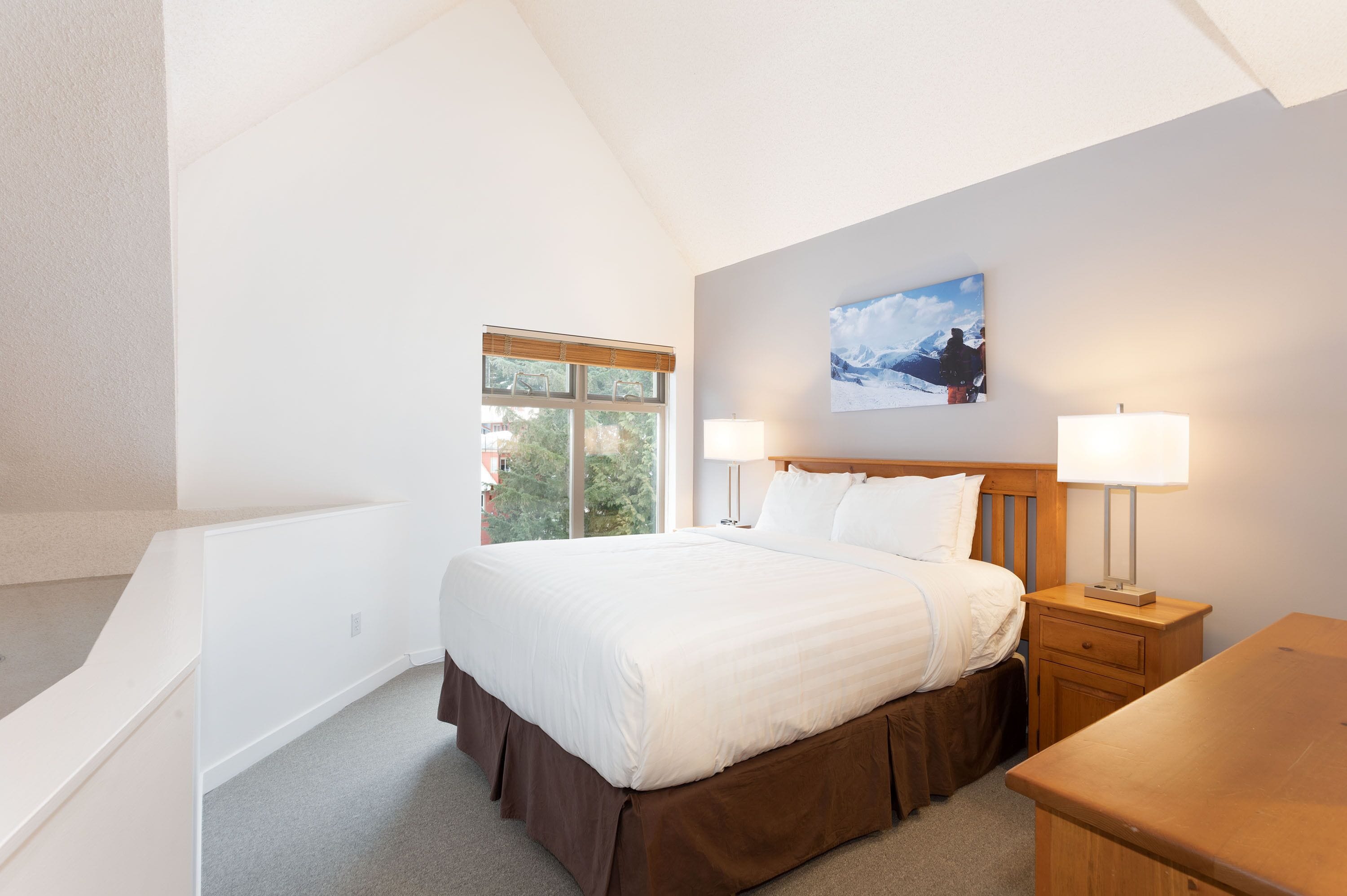 A bedroom with a large bed, two bedside lamps, a window, and a painting on the wall.