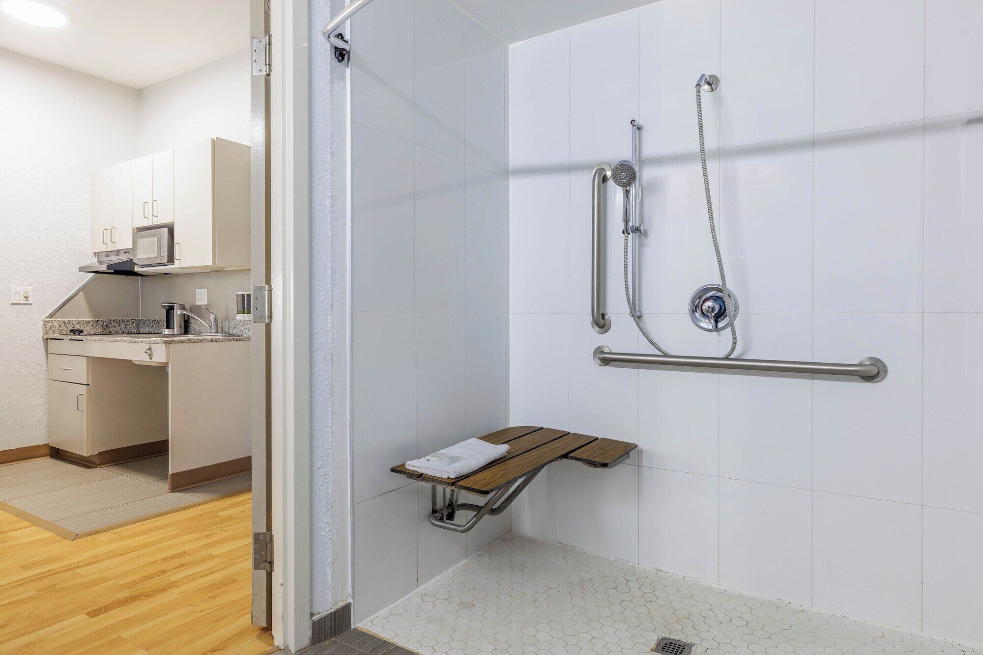 Une salle de bain moderne équipée d’une douche, de barres d’appui, d’un banc et d’un lavabo avec un plan de travail.
