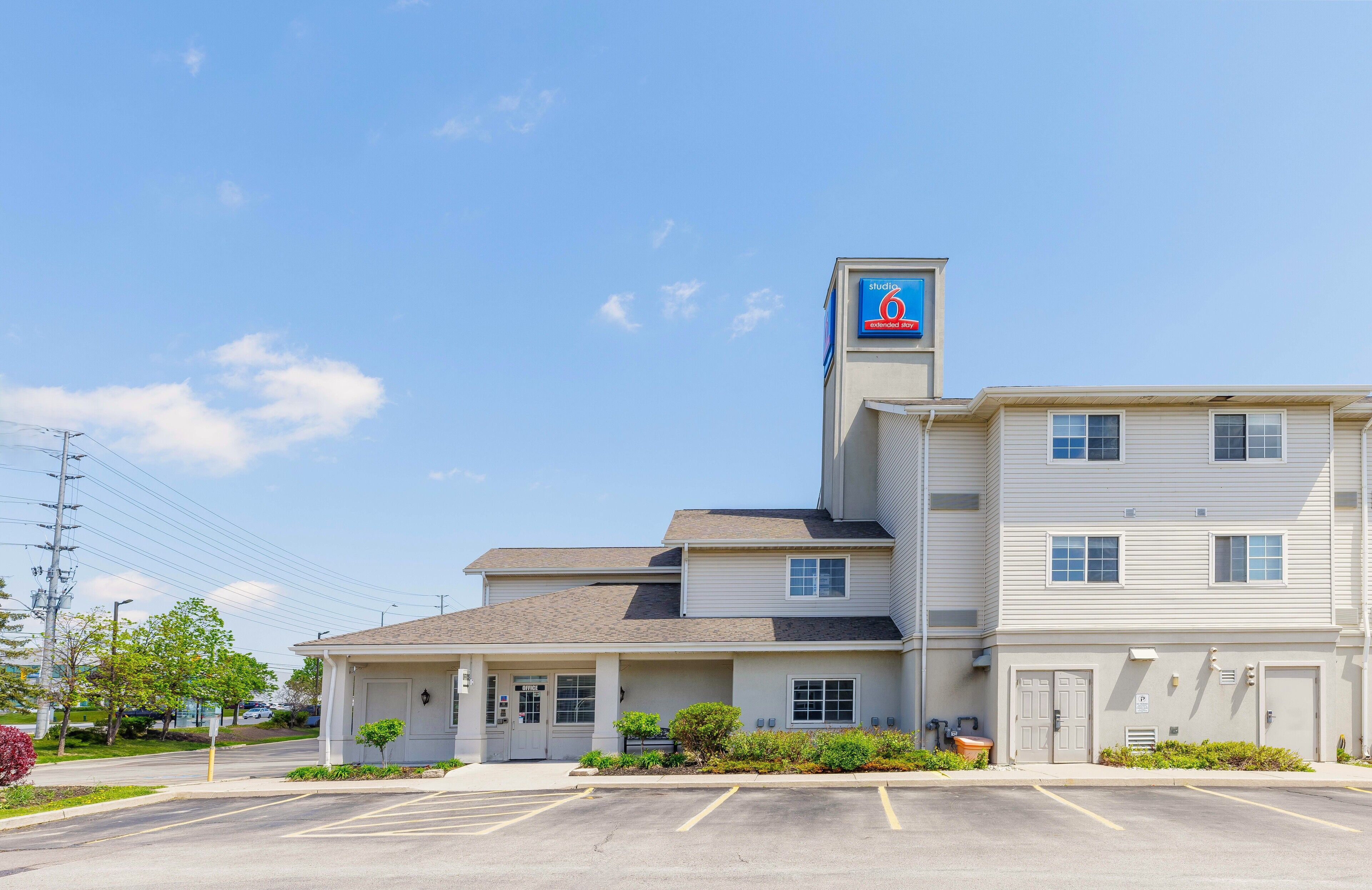 A motel with a prominent '6' sign on the roof, a parking lot, and a small front garden.