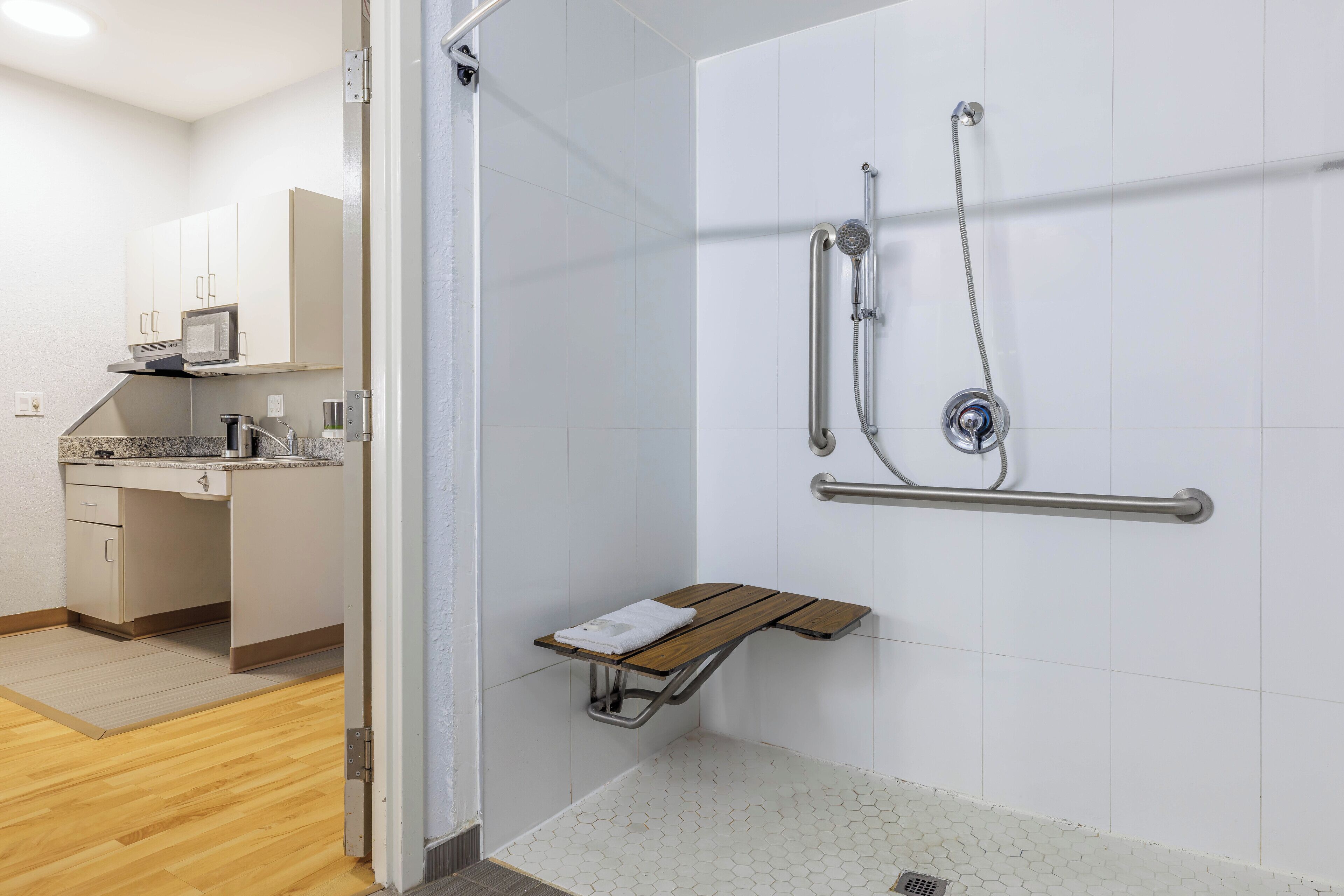 A modern bathroom with a shower, grab bar, and a small bench.