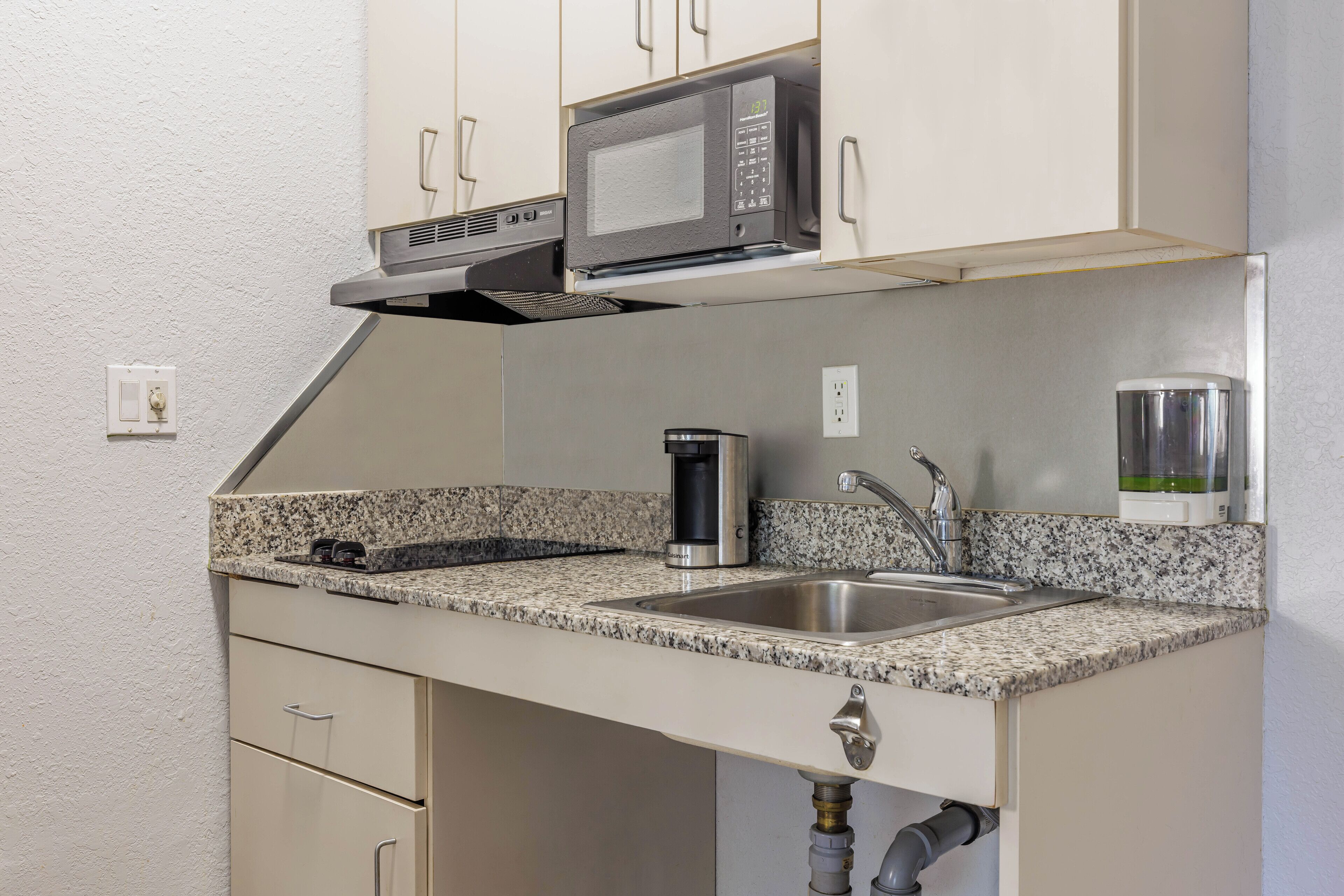 A compact kitchen with a microwave, sink, and coffee maker.
