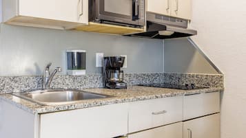 Cocina compacta con un lavamanos de acero inoxidable, microondas, cafetera y extractor de aire empotrado.
