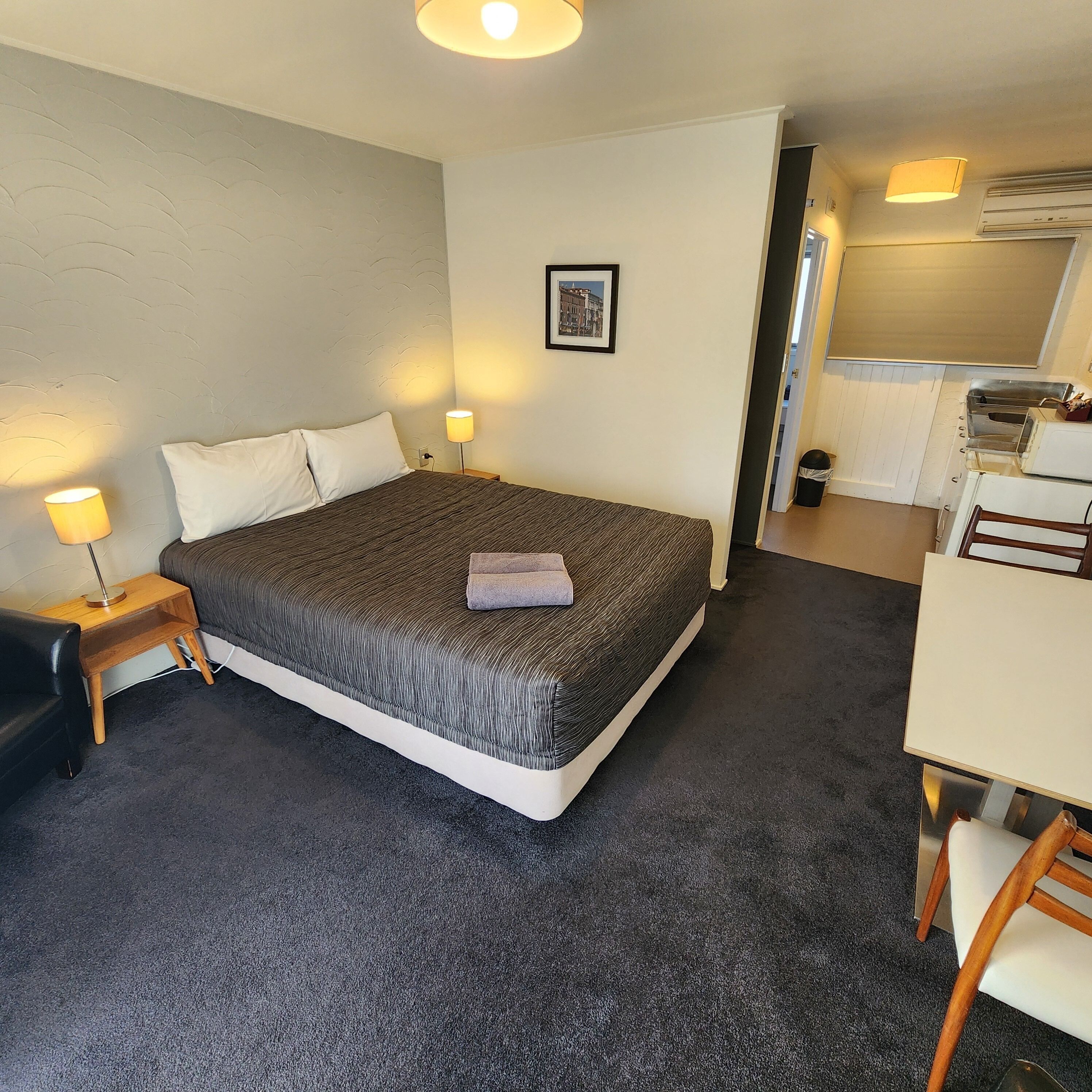 Ein Hotelzimmer mit einem Bett, Nachttischlampen, einem gerahmten Bild an der Wand und einer Küchenzeile.