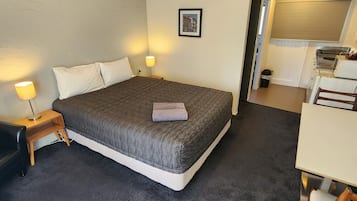 A hotel room with a bed, bedside lamps, a framed picture on the wall, and a kitchenette area.