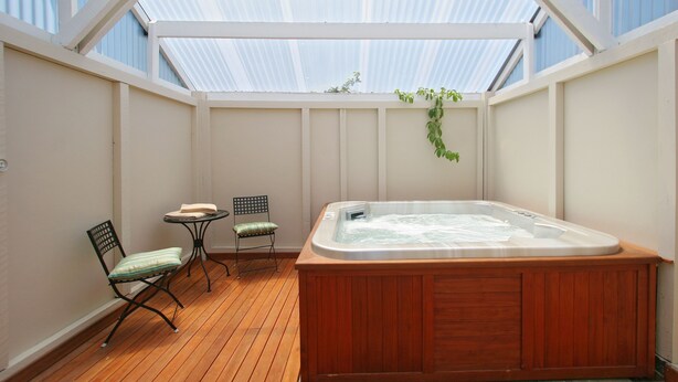 A hot tub in a sunlit room with wooden flooring, a small table, and two chairs.