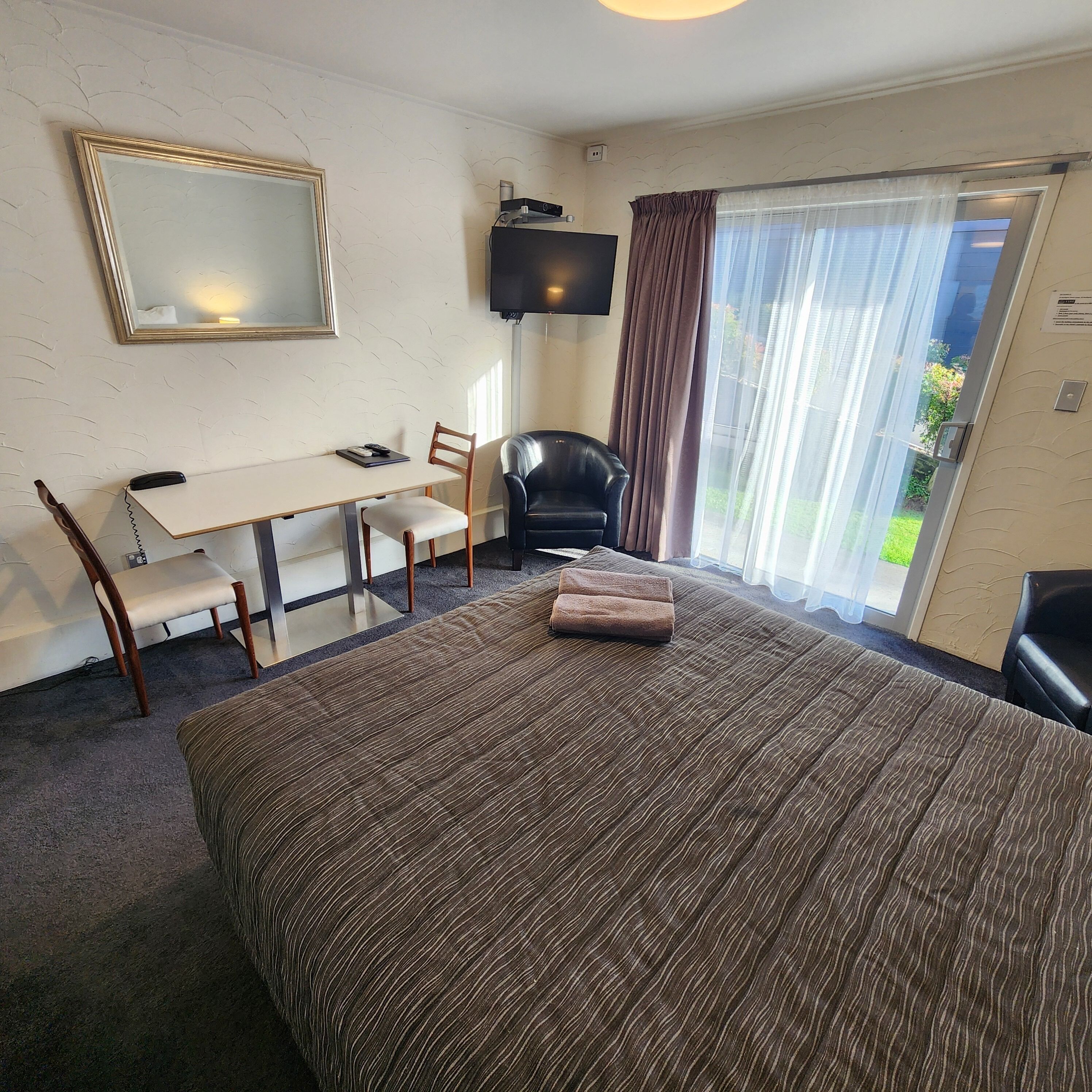 Habitación de hotel con cama, escritorio, silla, televisor y ventana con cortinas.