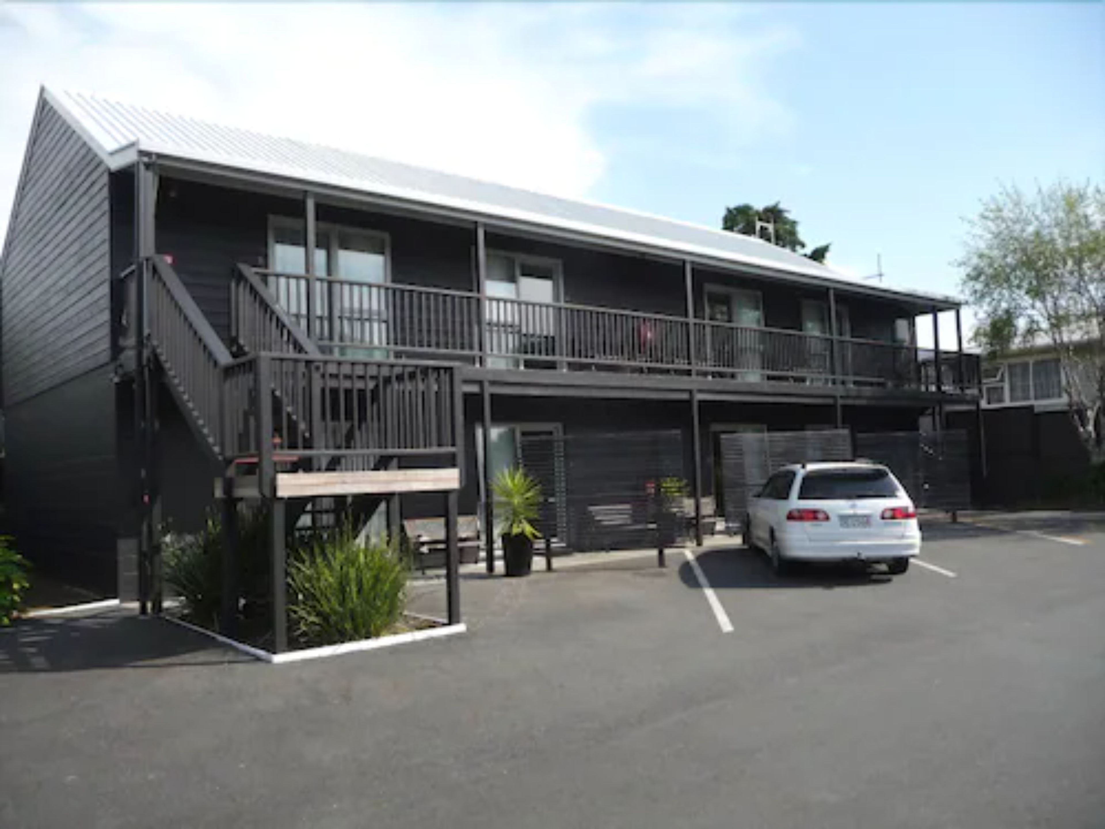 A two-story motel with a covered parking area and a white car parked in front.