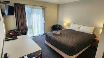 Quarto de hotel com cama, escrivaninha, cadeira, televisão e abajur.