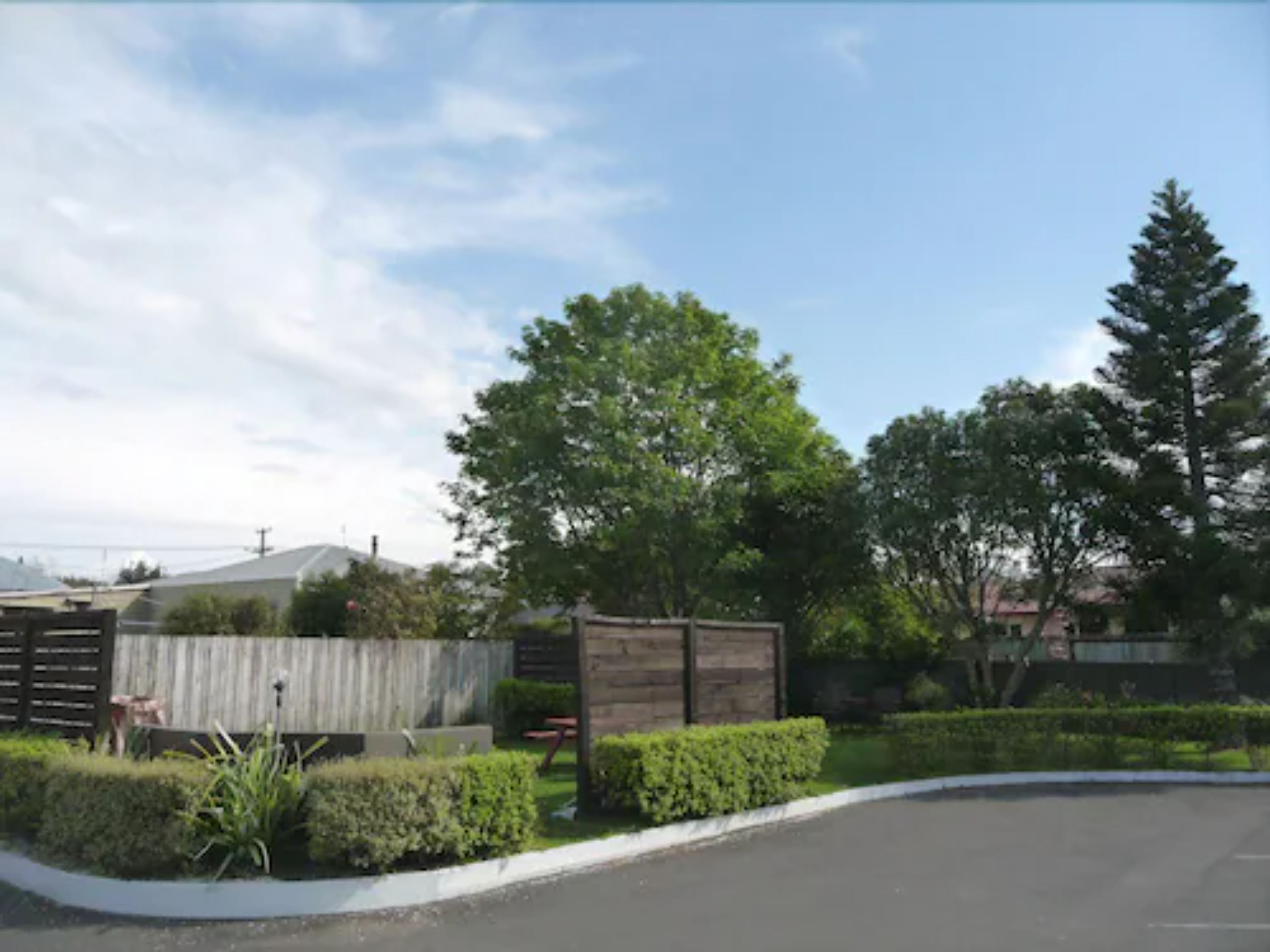 A parking lot with a curved road, surrounded by neatly trimmed hedges and a wooden fence.