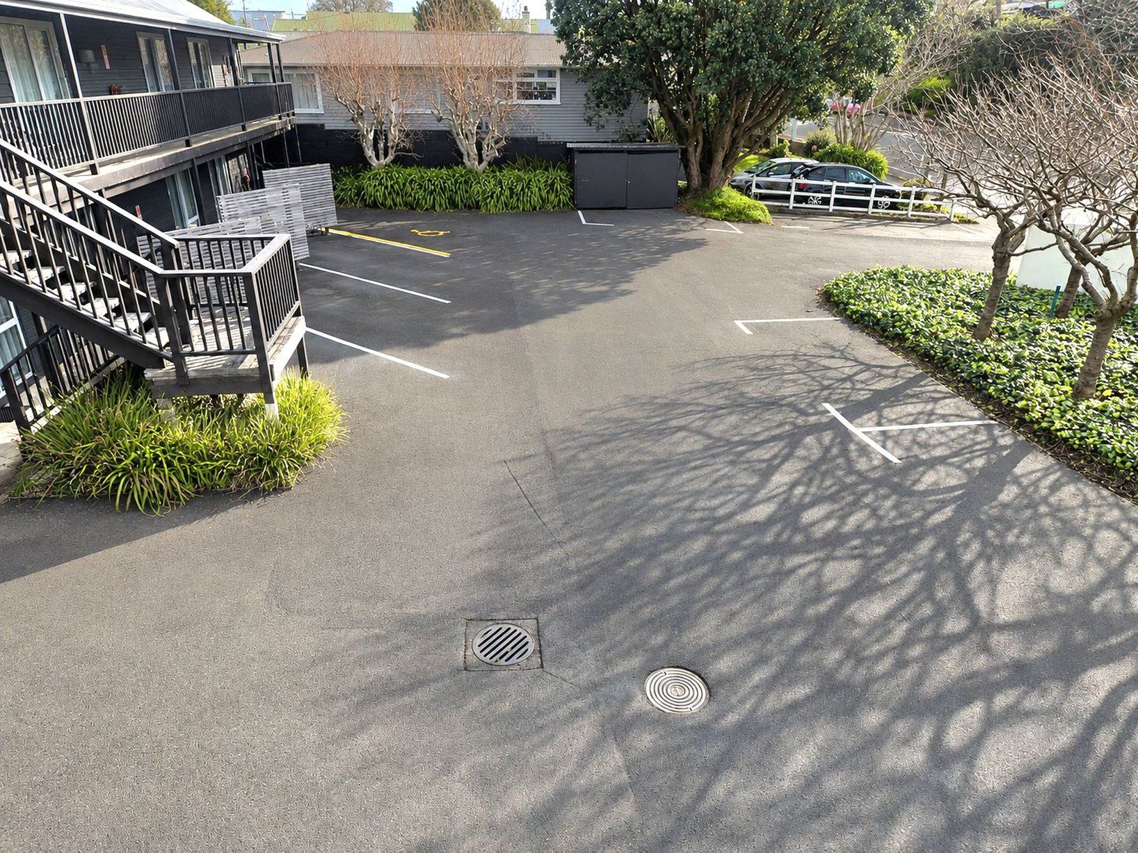 A parking area with marked spaces, a staircase, and a building with a balcony.