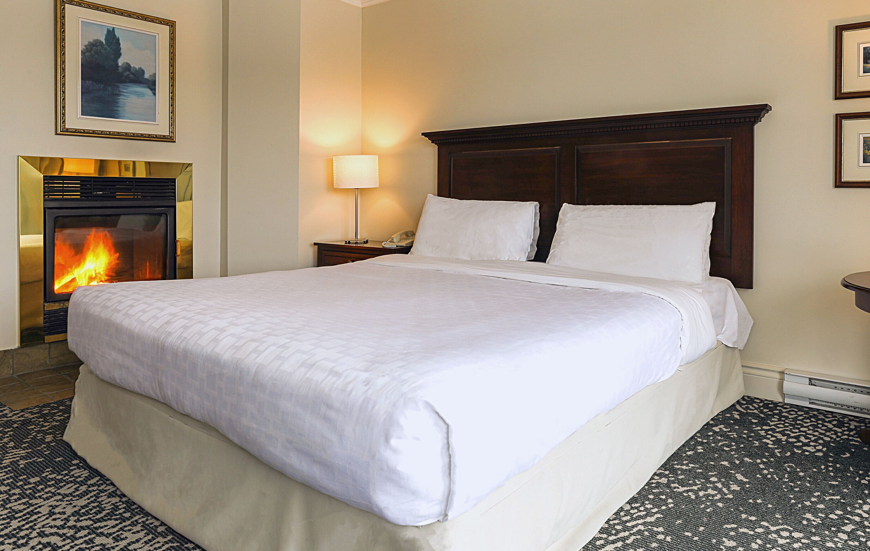 Een hotelkamer met een groot bed, een open haard en een nachtkastje met een lamp.