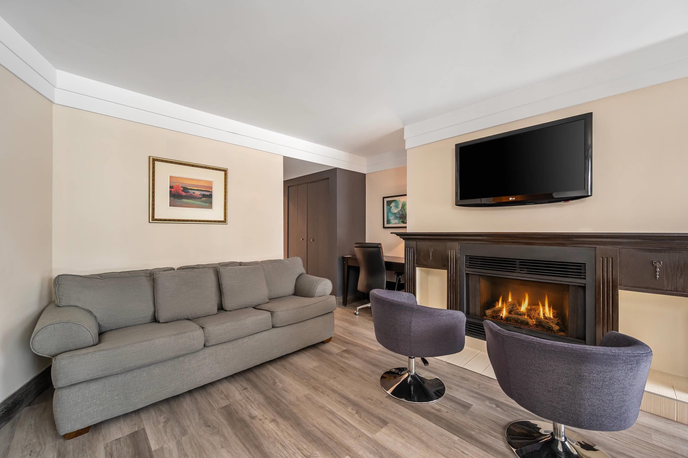 A living room with a sofa, two armchairs, a flat-screen TV, and a fireplace.